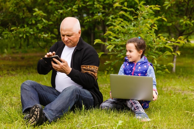 L'uomo anziano con sua nipote sta studiando un computer portatile all'aperto. Educazione su Internet per il vecchio nonno.