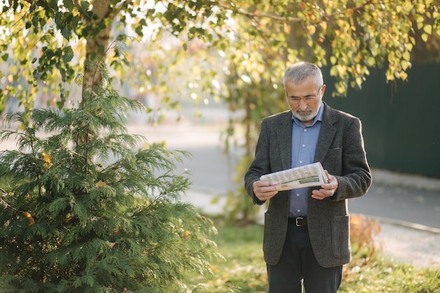 L'uomo anziano ha letto un giornale nel parco Sullo sfondo di un albero giallo in autunno