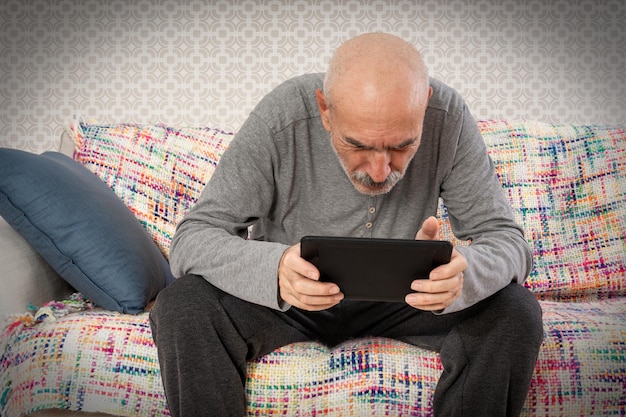 L'uomo anziano ha problemi con la vista mentre cerca di leggere o guardare qualcosa sul tablet