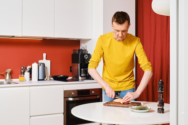 L'uomo anziano taglia la pelle su un petto d'anatra in cucina