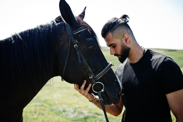 L'uomo arabo con barba alta indossa in nero con cavallo arabo