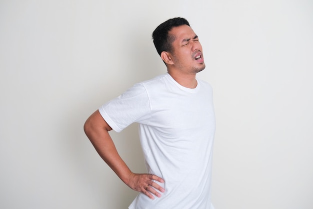 L'uomo asiatico adulto che indossa una maglietta bianca semplice soffre di lombalgia