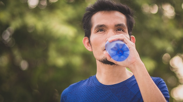 L'uomo asiatico beve acqua esercizio sportivo all'aperto
