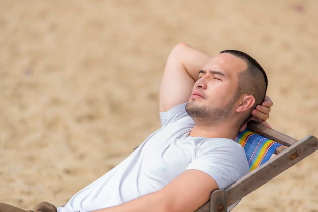 L'uomo asiatico che si siede sulla spiaggia della sedia all'interno del mare Tempo di relax in estate