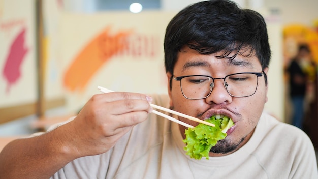 L'uomo asiatico con gli occhiali mangia una deliziosa lattuga nel ristorante