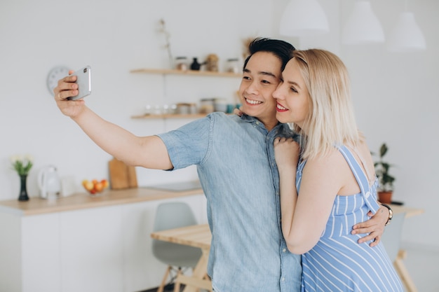 L'uomo asiatico e la sua donna bionda caucasica passano insieme il tempo e facendo selfie per l'altro in cucina