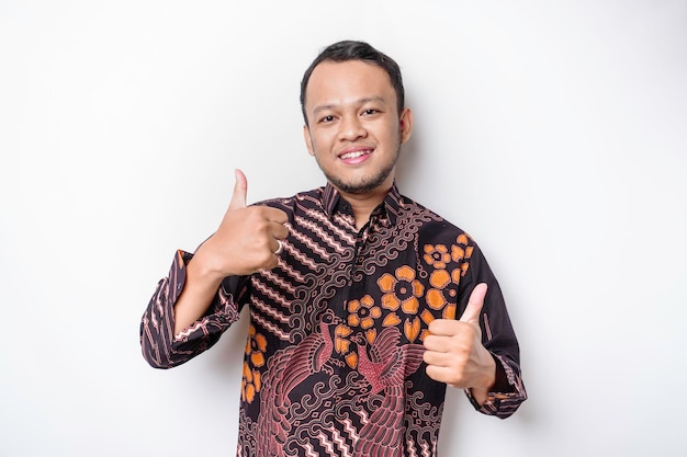 L'uomo asiatico eccitato indossa una camicia batik dà il pollice in alto gesto di approvazione isolato da sfondo bianco
