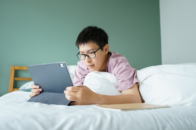 L'uomo asiatico gioca un computer portatile nel suo letto. Concetto di tecnologia