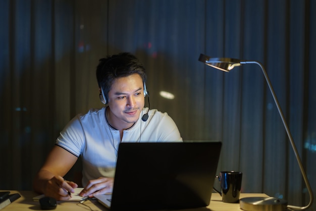 L'uomo asiatico lavora a casa è seduto al lavoro con colleghi o manager tramite videochiamata di notte a casa.