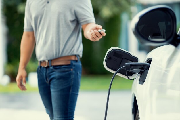 L'uomo asiatico progressista ricarica la sua auto EV alla stazione di ricarica domestica