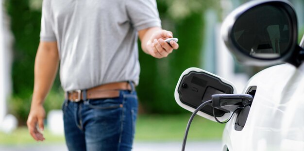 L'uomo asiatico progressista ricarica la sua auto EV alla stazione di ricarica domestica