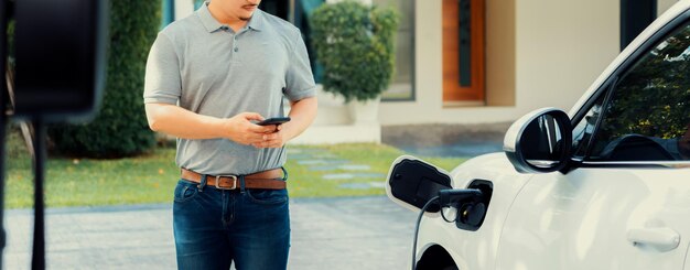 L'uomo asiatico progressista ricarica la sua auto EV alla stazione di ricarica domestica