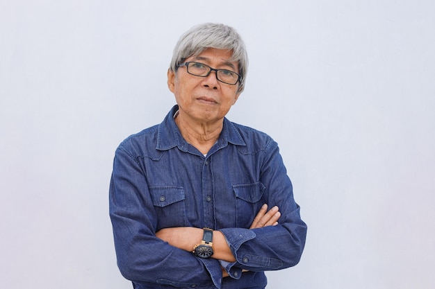 L'uomo asiatico senior dai capelli grigi in stile casual denim con le braccia incrociate guarda direttamente alla fotocamera con