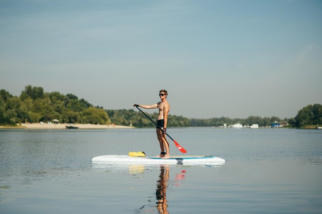 L'uomo atletico a bordo del sup è attivo sul fiume in una calda giornata estiva con in mano un remo e distoglie lo sguardo