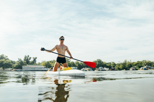 L'uomo atletico nuota su uno stagno in estate in una giornata di sole su una tavola da sup con un remo in mano