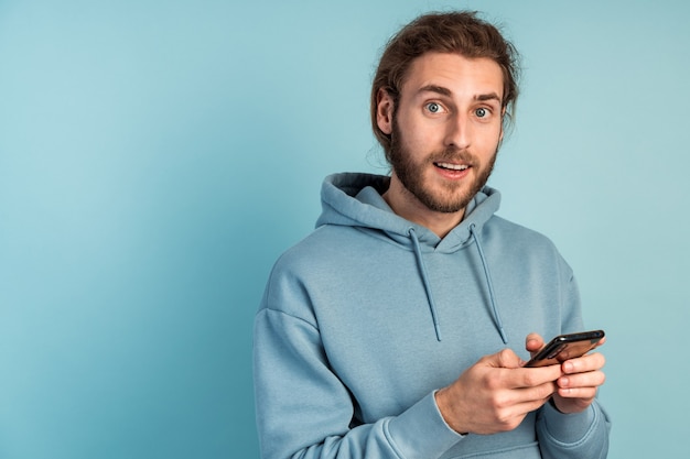 L'uomo attraente con la barba sta tenendo uno smartphone, è sorpreso da qualcosa.