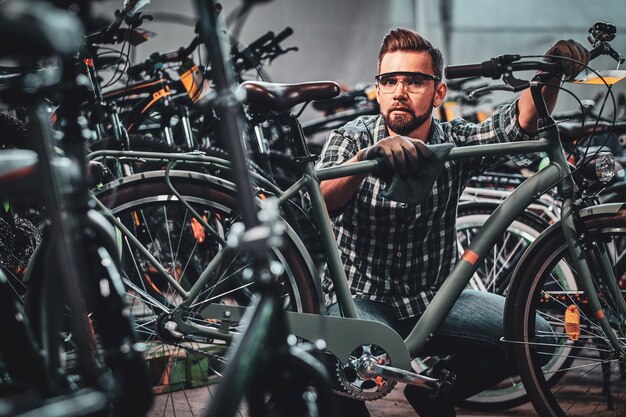 L'uomo attraente e impegnato con gli occhiali protettivi sta pulendo una bicicletta dalla polvere.