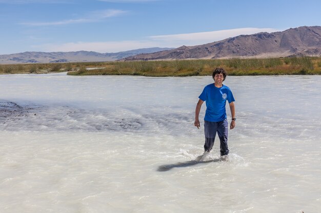 L'uomo attraversa a piedi un fiume di montagna bianca. Altai, Mongolia.