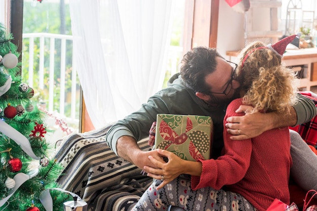 L'uomo bacia la donna a casa e le fa un regalo di Natale Condividendo il concetto di regalo di Natale Attività per il tempo libero a casa con una vera coppia felice che si abbraccia con amore e divertimento Vacanza di amore e relazione