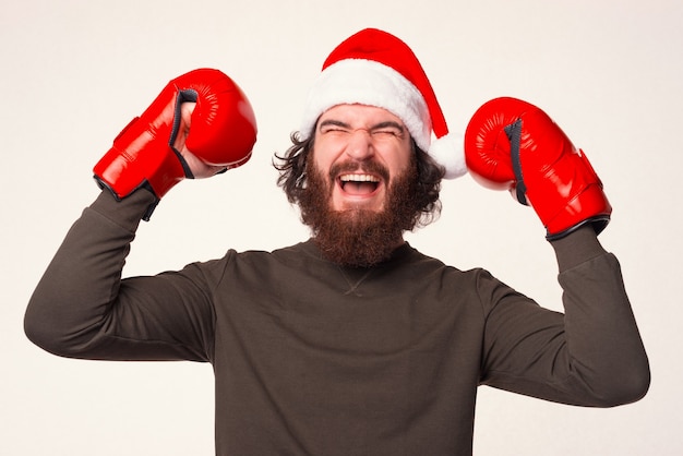 L'uomo barbuto che indossa un cappello natalizio e dei guantoni da boxe sta facendo il gesto del vincitore.
