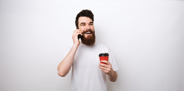 L'uomo barbuto che tiene una tazza porta via e parla al telefono.