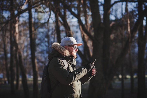 L'uomo barbuto con un berretto tiene in mano uno smartphone all'aperto