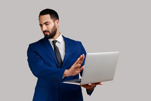 L'uomo barbuto confuso che chiude gli occhi con la mano evita di guardare contenuti vergognosi sul laptop