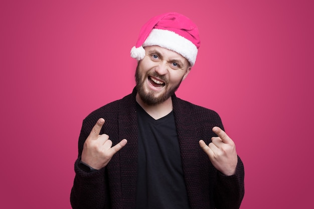 L'uomo barbuto di Casuca sta gesticolando il segno del rock and roll mentre sorride su un muro rosa che porta il cappello della Santa