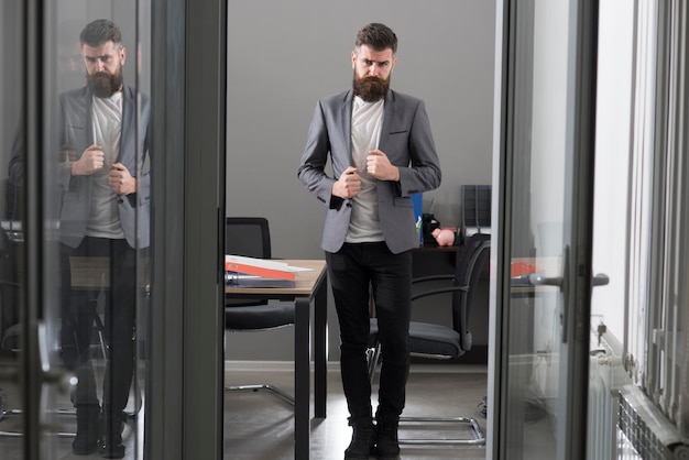 L'uomo barbuto di stile di vita di affari e d'ufficio guarda fuori dalla porta della stanza uomo d'affari in un ufficio moderno con vetro