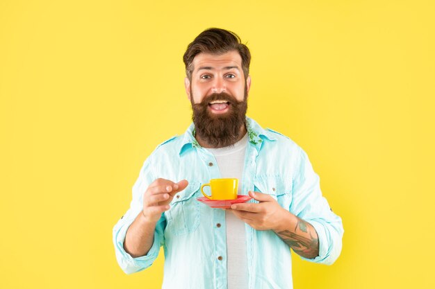 L'uomo barbuto felice beve il caffè del mattino su sfondo giallo caffè