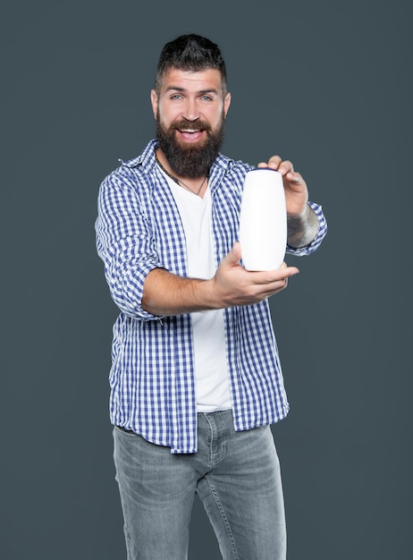 L'uomo barbuto felice tiene la bottiglia di shampoo del prodotto di bellezza