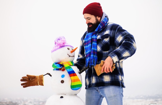 L'uomo barbuto in abiti caldi stringe la mano con pupazzi di neve moda inverno pupazzi di neve in guanti sciarpa cappello