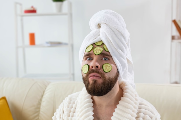 L'uomo barbuto si diverte con una maschera cosmetica sul viso fatta con fette di cetriolo per la cura della pelle e