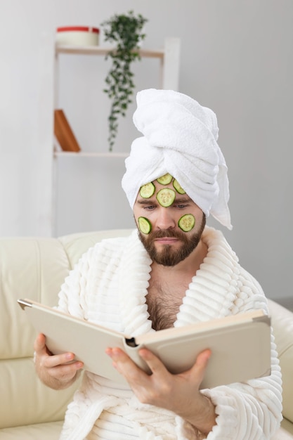 L'uomo barbuto si diverte con una maschera cosmetica sul viso fatta con fette di cetriolo per la cura della pelle e