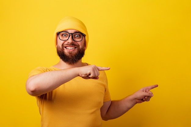 L'uomo barbuto sorridente con gli occhiali punta l'indice su sfondo giallo