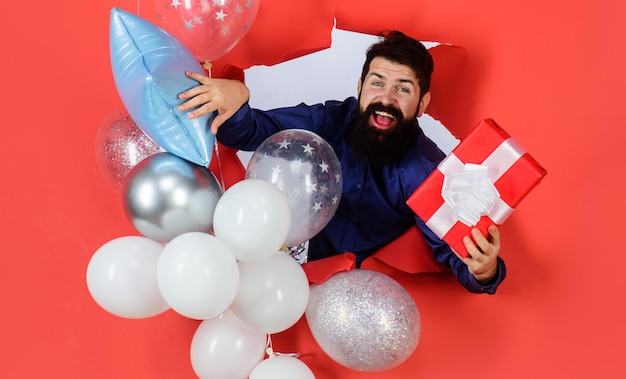 L'uomo barbuto sorridente della festa di compleanno con gli aerostati tiene l'anniversario di celebrazione di festa felice del regalo