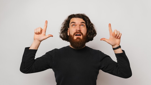 L'uomo barbuto stupito con i capelli lunghi punta sopra la sua testa con entrambe le mani