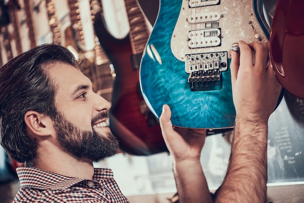 L'uomo barbuto torce il controllo del volume sulla chitarra elettrica in negozio.