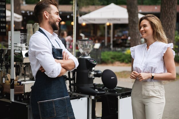 L'uomo barista e la sua cliente donna hanno una piccola conversazione durante la giornata estiva accanto alla caffetteria mobile.