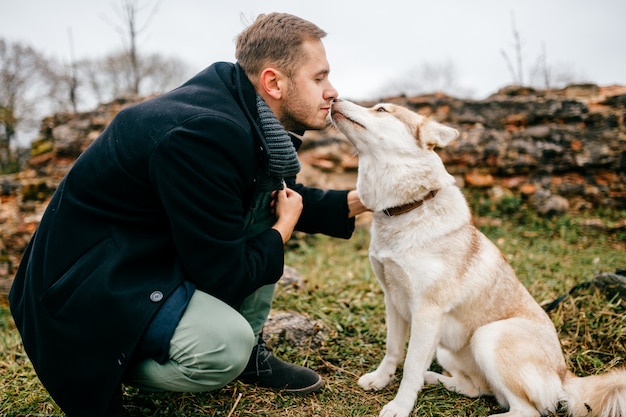 L'uomo bello adulto in vestiti di affari che cammina con il cucciolo di cane adorabile sveglio del husky all'aperto oltre il muro di mattoni del castello europeo rimane. Proprietario maschio con abbracci canini di razza pura. Ragazzo che abbraccia il suo cane