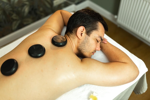 L'uomo bello del resort termale riceve un massaggio con pietre calde Terapia di massaggio con pietre calde