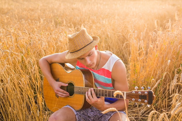 L'uomo bello felice sta suonando la chitarra nel campo