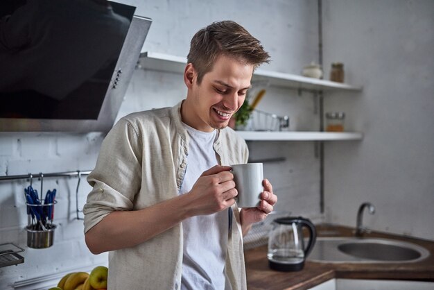 L'uomo bello in cucina sorride e beve caffè al mattino.