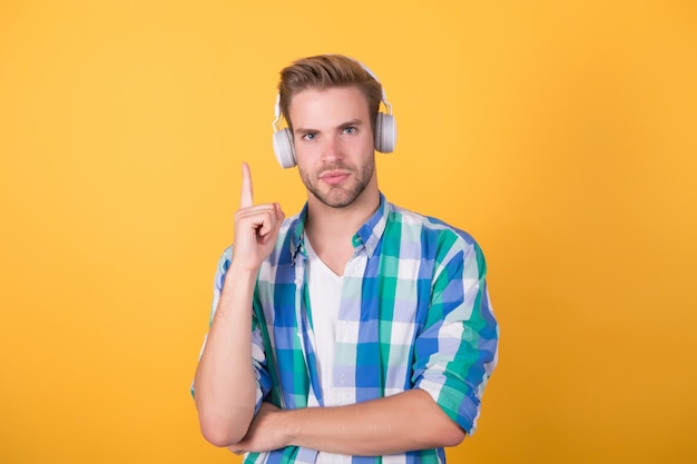 L'uomo bello indossa le cuffie tenendo il dito sollevato l'idea di sfondo giallo