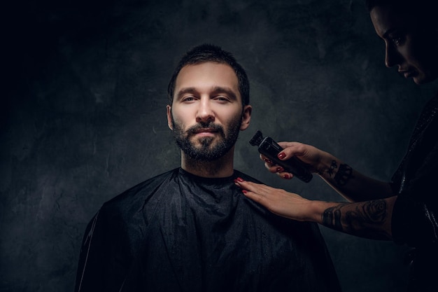 L'uomo bello si fa curare i capelli da una parrucchiera tatuata in uno studio scuro.