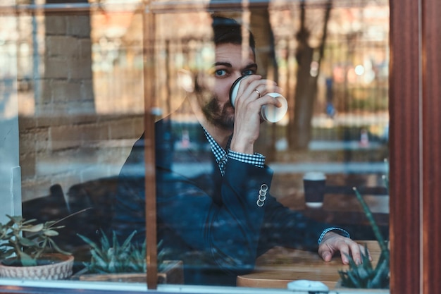 L'uomo bello si sta godendo il suo caffè mentre è seduto al bar vicino alla finestra.