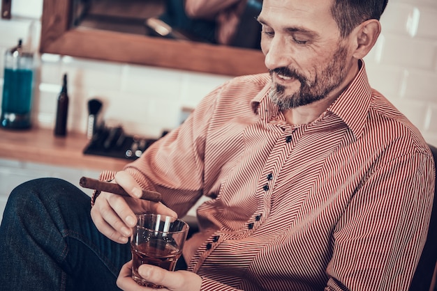 L&#39;uomo beve whisky e fuma una sigaretta in un negozio di barbiere