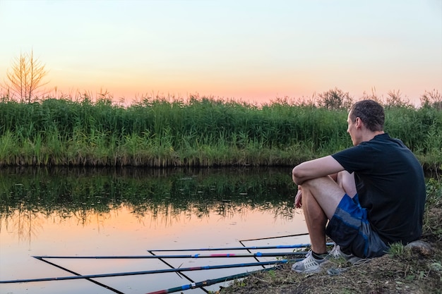 L'uomo calmo e rilassato pesca su un sacco di pesca mentre è seduto sulla riva del lago al tramonto