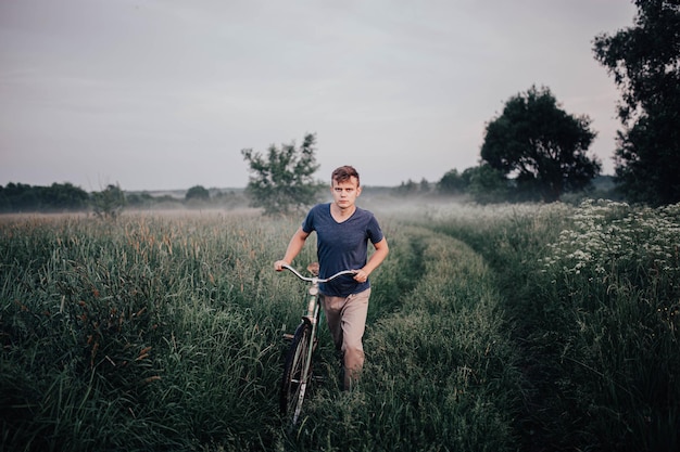 l'uomo cammina con una bicicletta retrò verde su una strada di campo e sull'erba in estate