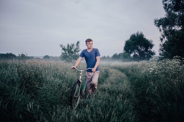 l'uomo cammina con una bicicletta retrò verde su una strada di campo ed erba in estate
